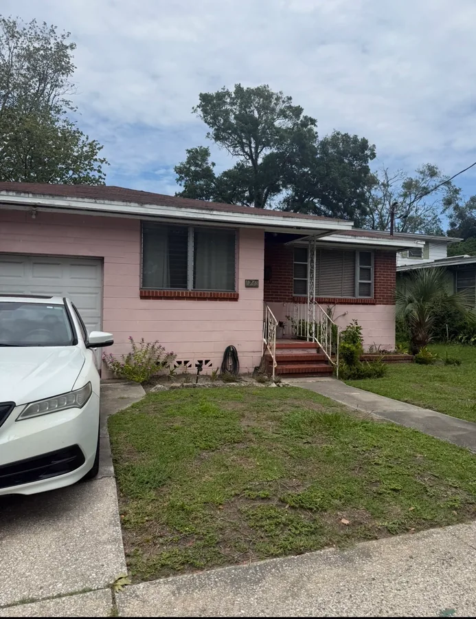 A pink family home with a green lawn and a car in the drive.