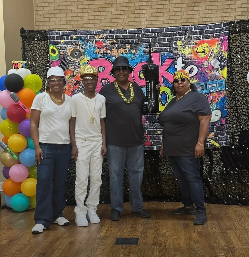 Four relatives posing in front of a colourful “Back to” party backdrop with balloons.