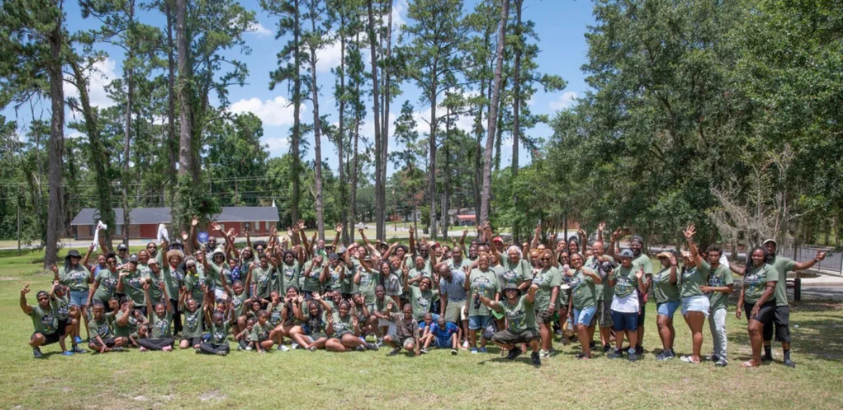 A large Edwards family reunion group in matching green shirts, arms raised, on a lawn under tall pines.
