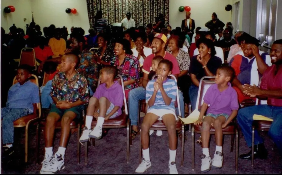 Children and adults watching from rows of chairs in a decorated hall.