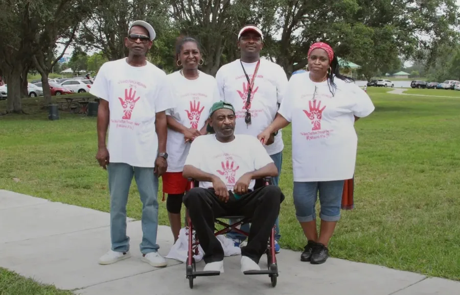 A smaller group in the white handprint reunion shirts, one seated in a wheelchair at the centre.