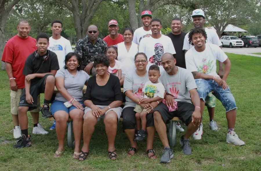 A big family group posed on a park lawn, the front row seated on a bench.