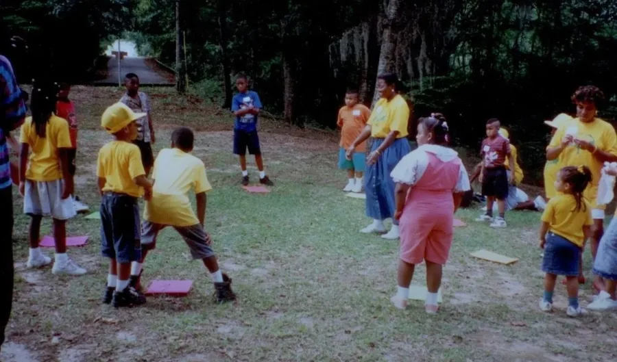 Kids in bright shirts running and playing games on a shaded lawn.