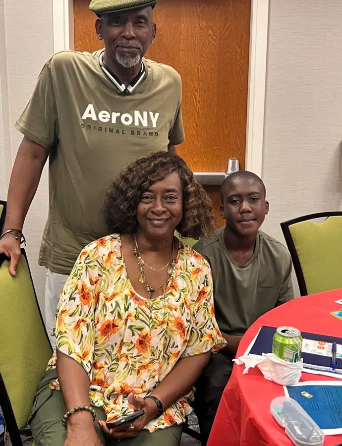 Three generations at a reunion table, a man standing behind a seated woman and a boy.